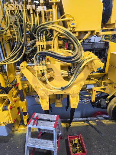 Gelbe Maschinenkomponenten mit Kabeln und Werkzeug auf dem Boden.